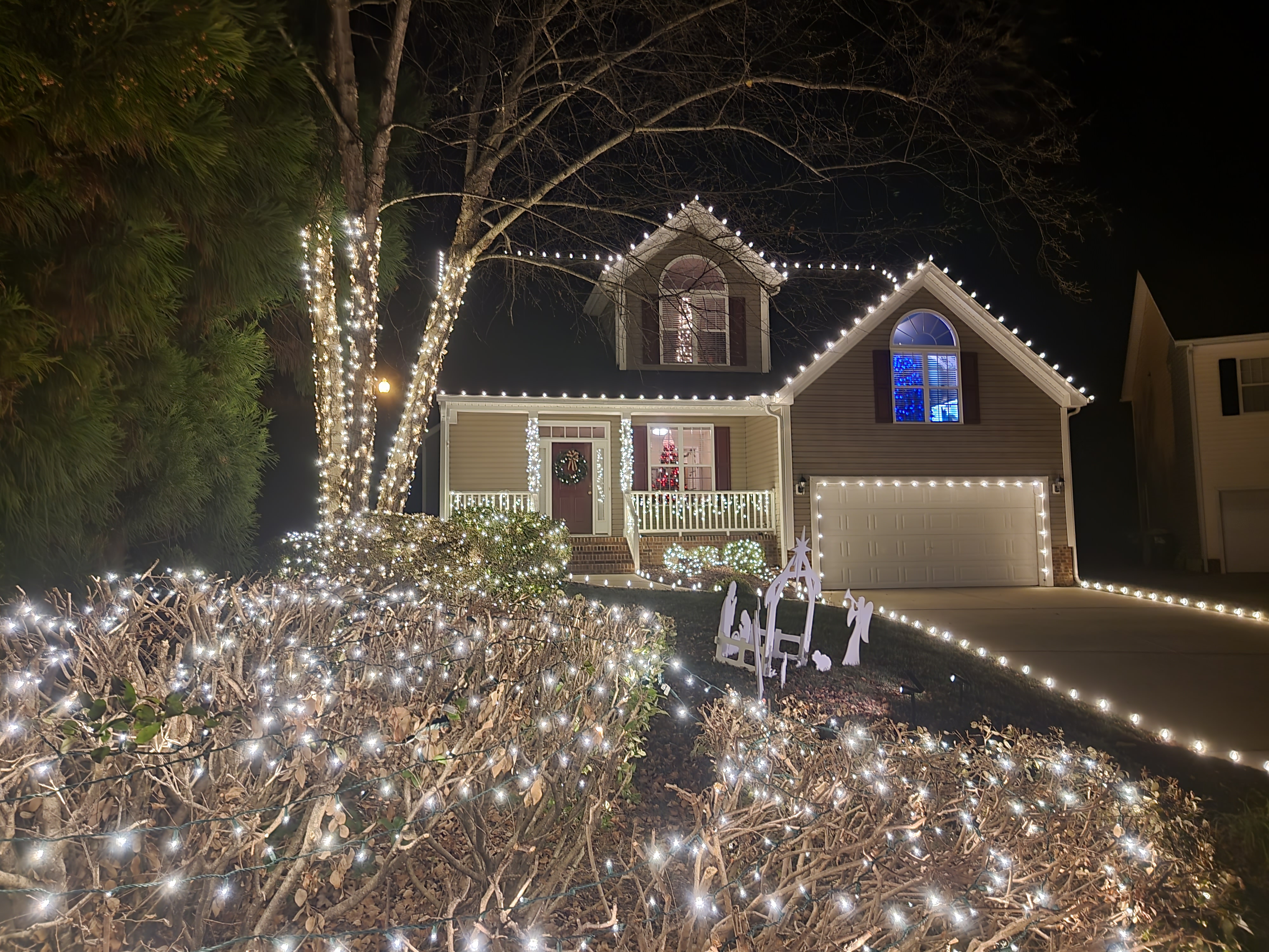 Beautiful Christmas light display on home - Professional holiday lighting installation by St Augustine Christmas Lights featuring warm white LED roofline lights, illuminated trees, landscaping lights, and garage door accent lighting creating a magical private Nights of Lights experience